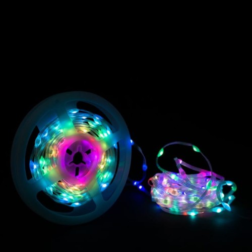 Taśma LED 200 4W RGB IP65 o długości 10 m, umieszczona na białym rolce. Widoczne kolorowe diody emitujące światło w różnych odcieniach, w tym zielonym, niebieskim i różowym. Taśma lekko zwinięta z jednego końca. Tło czarne.