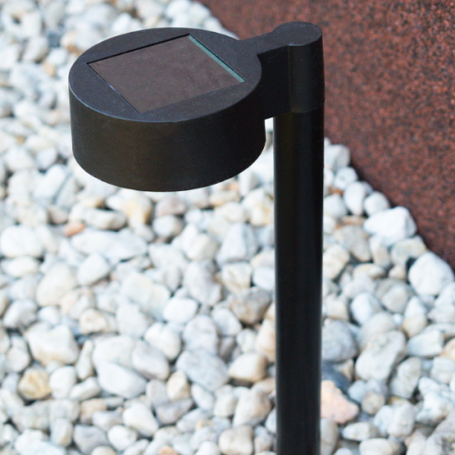 Lampa solarna EYE IP44, czarna, o wysokości 38 cm, z okrągłym kloszem i panelami słonecznymi na górze. Ujęcie pokazuje lampę na tle żwiru, w pozycji stojącej.