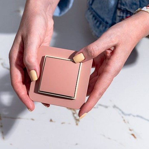 Szara ramka pośrednia Karlik MINI (27MRP-1) w rękach użytkownika. Produkt o prostokątnym kształcie z delikatnym, matowym wykończeniem i subtelnymi złotymi krawędziami. Ujęcie z przodu, na jasnym tle.