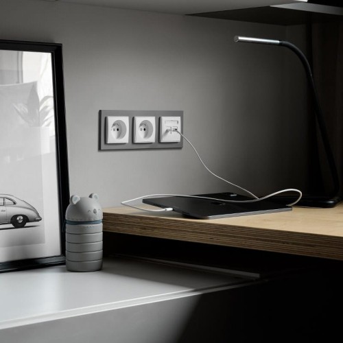 Aranżacja produktów Karlik MINI w kolorze taupe i białym, ramka potrójna umieszczona na ścianie. Widoczne dwa gniazda elektryczne, kabel podłączony do gniazda komputerowego. Minimalistyczne otoczenie biurowe z drewnianym blatem.