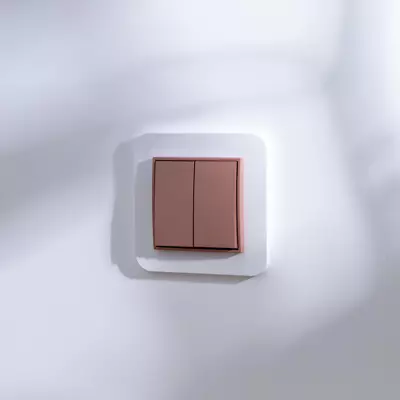 Łącznik żaluzjowy Karlik MINI w kolorze łososiowym, z dwoma przyciskami, zamontowany na białej ramce. Produkt widoczny frontowo na jasnym tle, w prostokątnej formie.