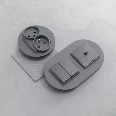 Wypust kablowy Karlik MINI w kolorze szarym matowym. Zestaw zawiera gniazdko podwójne oraz dwa przyciski w owalnej obudowie. Widoczna struktura materiału, prosty, nowoczesny design. Produkt leży na szarym tle.
