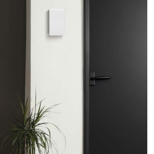 Dzwonek gong dwutonowy Orno Brevis Mini 230V w kolorze śnieżnobiałym, zamontowany na jasnej ścianie obok czarnych drzwi. Prosta, prostokątna forma, bez widocznych napisów czy logo, w otoczeniu rośliny doniczkowej.