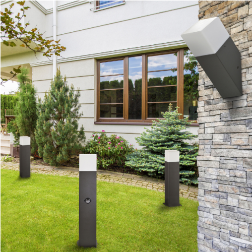 Lampa ogrodowa stojąca New York o wysokości 44 cm, z grafitowym korpusem i białym kloszem. Produkt umieszczony na trawniku, otoczony zielenią. Widoczne gniazdo na jednym z modeli. Tło zbudowane z domu i kamiennego muru.