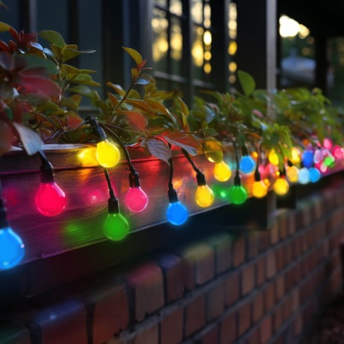 Żarówka LED KULKA E27 1W w kolorze czerwonym, o okrągłym kształcie, zamocowana na przewodzie z innymi kolorowymi żarówkami. Widoczna w aranżacji z roślinami na tle drewnianej skrzynki, oświetlająca otoczenie w ciepłej atmosferze.