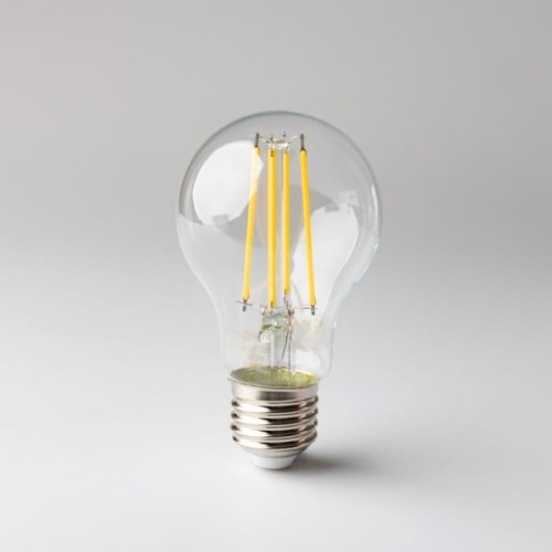 Żarówka LED filament E27 8W w kształcie tradycyjnej bańki, z przezroczystą szklaną obudową. Wewnątrz znajdują się cztery żółte włókna LED. Podstawa E27 metaliczna, na jasnoszarym tle. Emituje ciepłe białe światło.