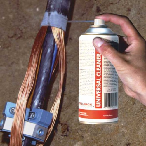 Środek czyszczący Universal Cleaner w sprayu 400 ml trzymany w ręku, skierowany na kabel. Butelka z białą etykietą i czerwonym napisem UNIVERSAL CLEANER, z widoczną częścią metalowego końcówki spryskiwacza. Tło w odcieniach brązu.