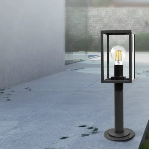 Lampa ogrodowa słupek MALMO E27 o wysokości 48 cm w kolorze grafitowym. Konstrukcja z metalowym stelażem w formie prostokątnej obudowy z przezroczystym kloszem. Ustawiona na okrągłej podstawie, idealna do oświetlenia przestrzeni zewnętrznych.