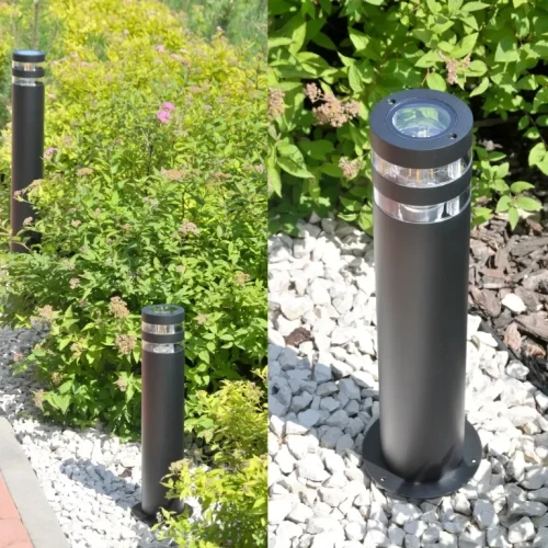 Lampa ogrodowa słupek RINO o wysokości 44 cm, okrągła, w kolorze czarnym, z przezroczystymi akcentami u góry. Stoi na białych kamieniach, otoczona zielonymi roślinami. Widoczne mocowanie podstawy. Idealna do oświetlenia ścieżek w ogrodzie.