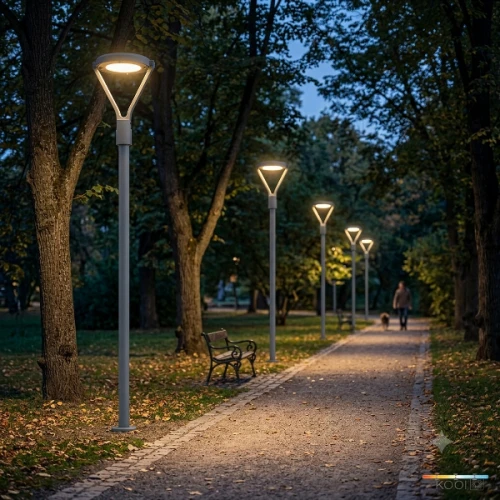 Lampa parkowa KOBI LED NEXPARK G2 o kształcie trójkątnym, montowana na wysokich słupkach. W oświetlonym parku, wzdłuż ścieżki, obok ławki. W tle spacerująca osoba z psem, otoczenie z drzewami i opadłymi liśćmi. IP66, dostępna w mocach 30W/40W/60W.