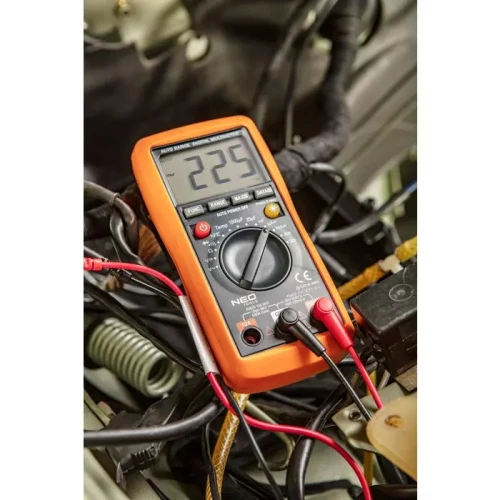 Miernik elektroniczny Neo 94-001 w kolorze pomarańczowym, z wyświetlaczem pokazującym wartość 225. Urządzenie leży na kablach w otoczeniu elementów elektrycznych, z widocznymi przyłączami pomiarowymi w kolorze czerwonym i czarnym.