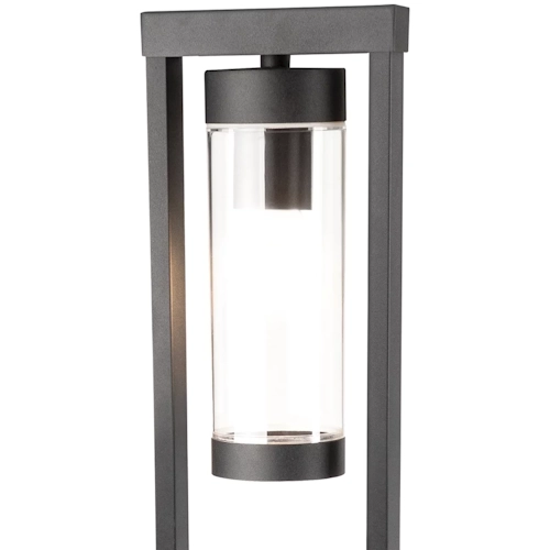 Lampa ogrodowa stojąca SPECTRA o wysokości 50 cm, w kolorze czarnym. Posiada prostokątną, stalową ramę oraz przezroczystą, cylindryczną osłonę na żarówkę. Ujęcie z przodu, ukazujące źródło światła wewnątrz.