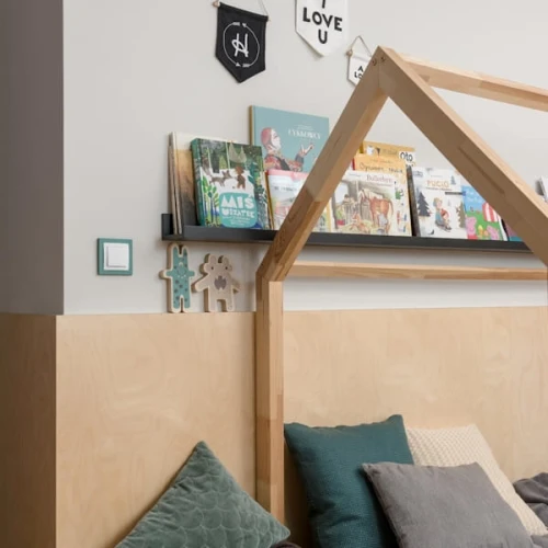 Ramka pojedyncza Karlik Deco w kolorze miętowym, kwadratowa, umieszczona na jasnej ścianie obok drewnianej półki z książkami. W tle widać tekstylia w stonowanych kolorach oraz dekoracje w kształcie postaci. Ramka jest zamontowana na ścianie.