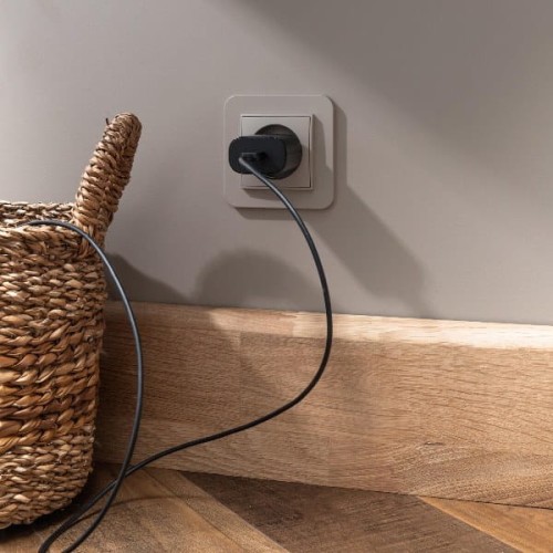Ramka pojedyncza Karlik MINI w kolorze taupe, zaokrąglona, zamontowana w gniazdku. W tle widoczny pleciony kosz oraz podłoga z drewnianych desek. Kabel z wtyczką podłączony do ramki, leżący na podłodze.